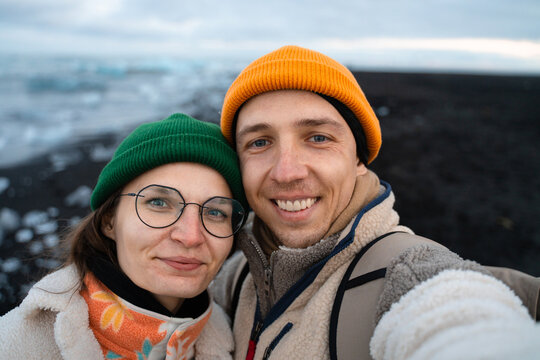 Joyful couple in love capturing selfie on black sand beach at ocean 
