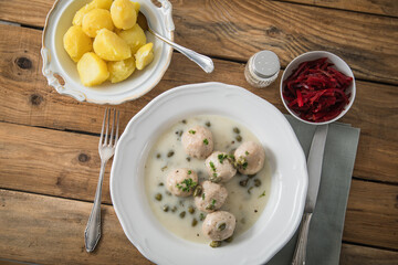 Königsberger Klopse mit Kapern, Salzkartoffeln und Rote Beete Salat auf tiefer Teller und rustikalen Holztisch mit Besteck, Salz und Serviette