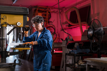 Focused mature woman working at metal factory