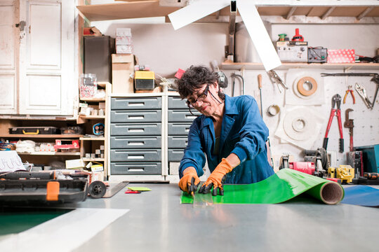 Happy mature worker cutting vinyl stickers at factory