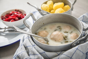 Königsberger Klopse mit Kapern im Topf, Salzkartoffeln und Rote Beete Salat auf Emaille Teller und grauen Stein Hintergrund mit Besteck und Tuch