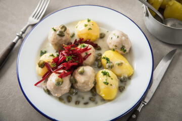Königsberger Klopse mit Kapern, Salzkartoffeln und Rote Beete Salat auf rustikal Emaille Teller und grauen Stein Hintergrund mit Besteck