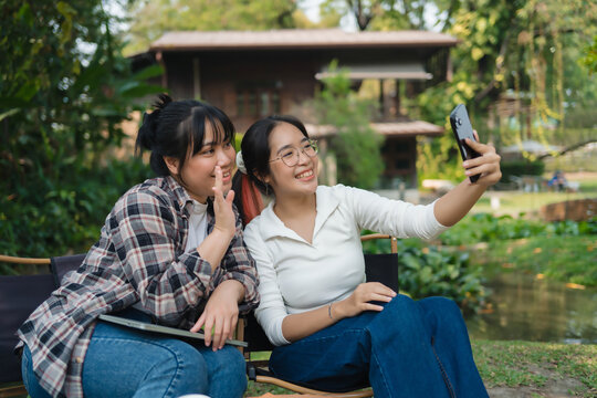 Two women sitting on a bench, one of them taking a picture of the other