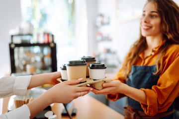 Female barista giving order to client, coffee in cardboard cups. Takeaway food concept.