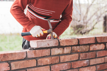 a man builds a brick wall, puts a brick on a cement-sand mortar, tapping on the brick with a construction hammer
