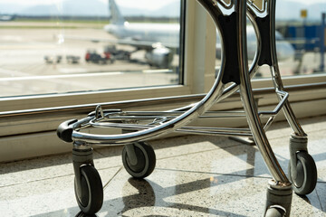 Small luggage cart in front of an airport window with a plane loading suitcases before taking off...