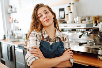 Young woman cafe owner in an apron looks at the camera and smiles. Business concept. Food and drink...