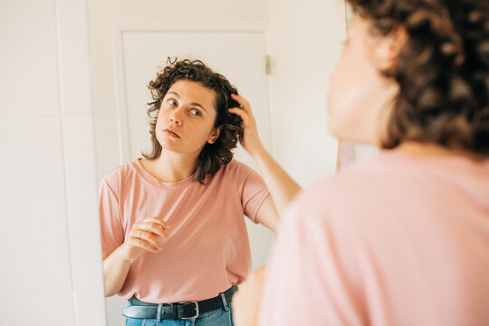 Woman in the mirror combing her hair with hand