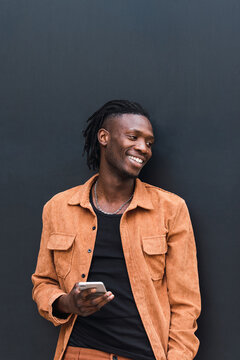 Cheerful black man browsing smartphone near wall
