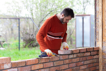 a man builds a wall of bricks, lays a brick on a cement sand mortar