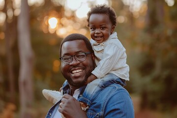 dark-haired man carries his son on his shoulders, both show a smile - obrazy, fototapety, plakaty