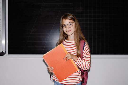 Schoolgirl with copybooks near chalkboard 