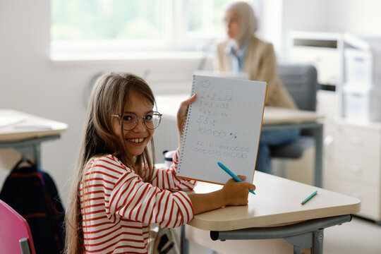 Smart and delighted pupil demonstrating solutions to tasks