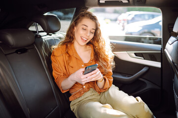 Young woman uses a smartphone while sitting in the back seat of a car. Concept of technology,...