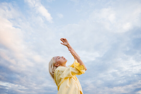 A woman raises her arms and head against the sky