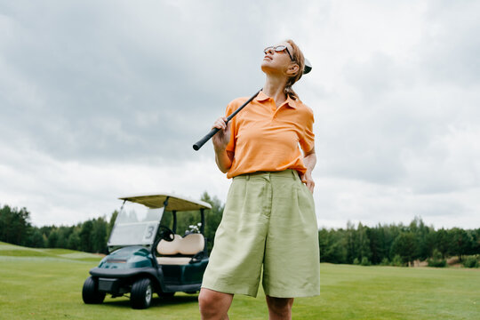 A woman with a golf club stands on a court
