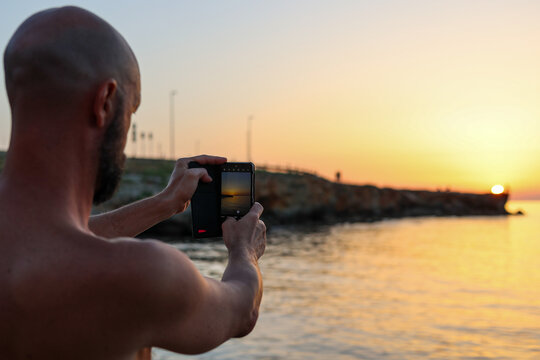 Naked tourist take a photo of the sunset during his trip by the sea