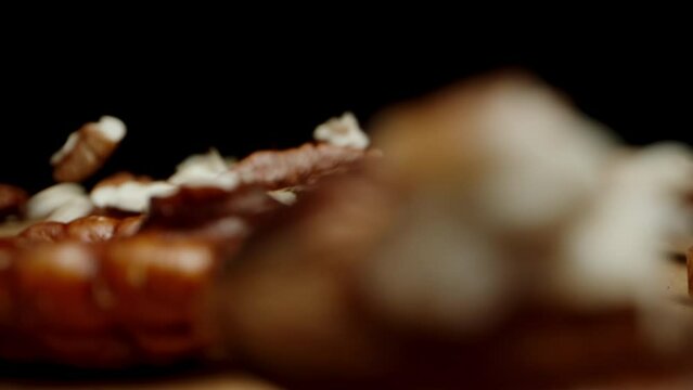 Peeled pecan nuts fall onto the table against a black background, close-up, slowed down.