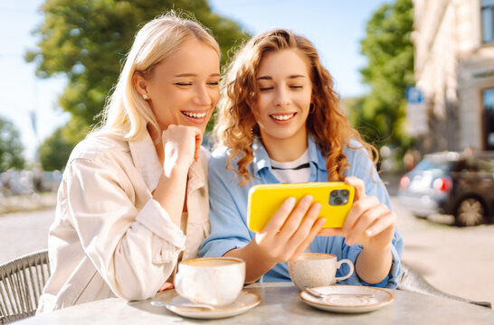 Two smiling woman are sitting in a cafe, drinking coffee, taking selfies, talking with friends. Fashion, beauty, blogging, tourism.