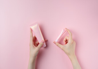 A woman's hand holds two pink tubes on a pastel pink background