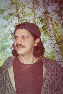Man with a mustache wearing a cap - trees and nature in the background