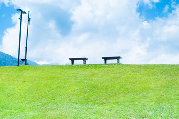 Wooden bench in green grass on slope with clouds and blue sky,Beautiful green hills, pastures and...