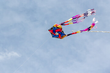 large kite of different colors flying in the blue sky winds