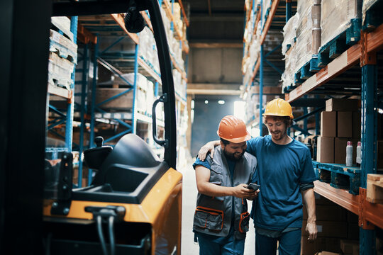 Smiling male coworkers using smartphone together in warehouse