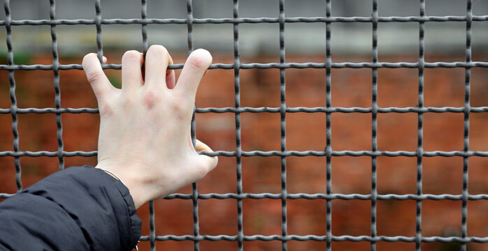 Iron bars of a reformatory and the hand of a man clinging to the fence