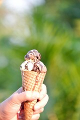 A soft cone of melting ice cream on male hand with sunlight and blurred a building background 