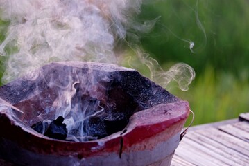 An old style brazier with hot coal and smoke in outdoor, blurred green nature background 
