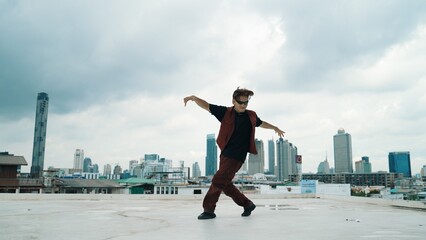 Fototapeta na wymiar Motion shot of B-boy dance performance by professional street dancer at rooftop with sky scrapper, city view. Attractive asian hipster show energetic footstep. Outdoor sport 2024. Endeavor.