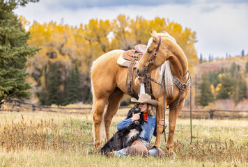 Colorado Cowgirl with a palomino horse and her herding dog in the mountains with colorful aspens in the background