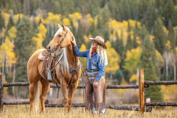 Blonde Cowgirl on a Palomino Horse in the Colorado Rocky Mountains in the Fall with Aspens in the...