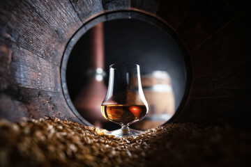 A glass of bourbon whiskey in old oak barrel. Copper alambic and oak barrel on background. Traditional alcohol distillery concept - 753848553