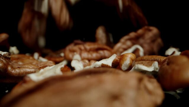 Peeled pecan nuts falling in slow motion onto a black reflective table. Dolly slider, close up.