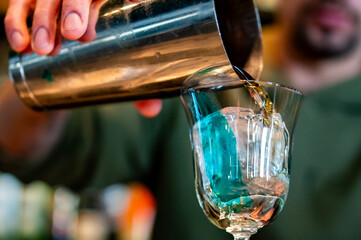 A bartender pours a vibrant blue cocktail into a clear glass, capturing the motion and vivid color....