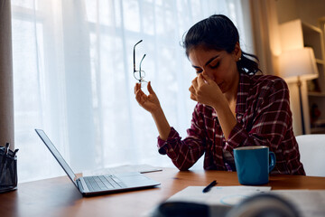 Stressed woman having  headache while working remotely on laptop at home.
