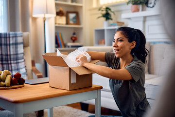 Happy Hispanic woman unboxing home delivered package.