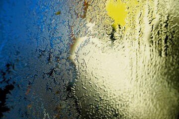 Abstraktes Motiv mit Eis- und Wassermuster auf Glasscheibe vor beige-gelbem Haus und blauem Himmel...