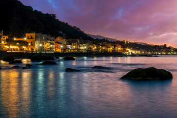 evening or night landscape of evening town coastline in golden lights and sea gulf with calm water and nice reflections with beautisul sunset sky on background