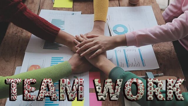 Equipo de trabajo uniendo sus manos festejando el trabajo en grupo, sobre escritorio con gráficos de barras, coloridos pullovers. Teamwork con letras formadas con balones de fútbol.