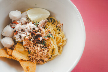 Egg noodles dried egg noodles with lime, minced pork, meatballs, and fried dumplings in white bowl....