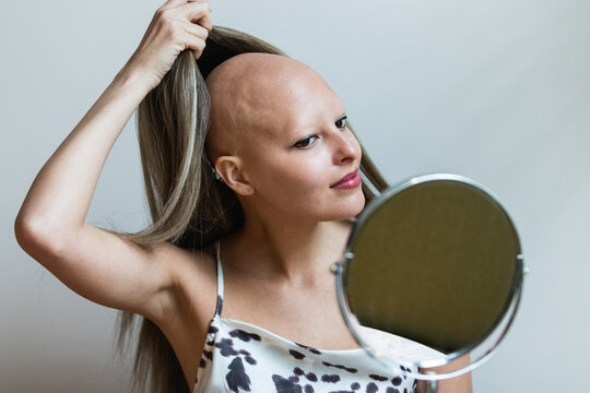 Young woman taking off wig and looking in mirror