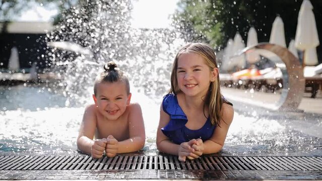 Children bathe and frolic in the pool in the summer, splashing water. Activity nature leisure. Sister and brother have fun in swimming pool