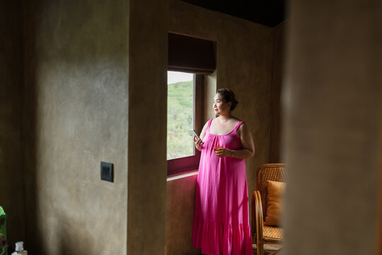Woman talking on cellphone standing near window looking aside
