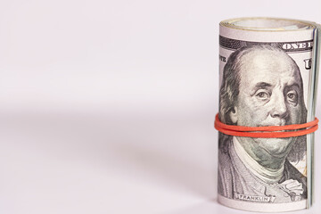 A stack of hundred-dollar bills tied with a red rubber band on white background.