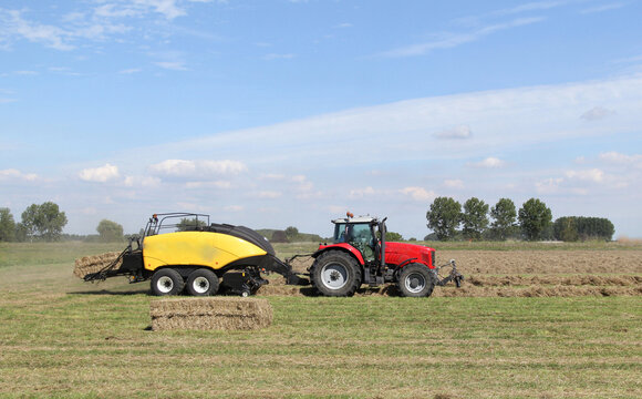 a tractor with a big baler is making big square straw bales in a field in the dutch countryside in summer