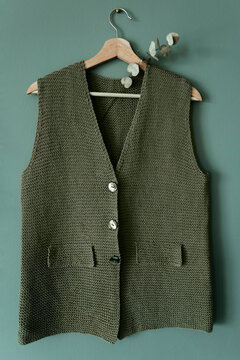 Knitted green vest on hanger.