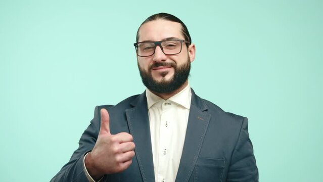 A bearded businessman in a smart suit gives a thumbs-up, his smile expressing approval and positivity, posed against a light teal backdrop. Camera 8K RAW. 